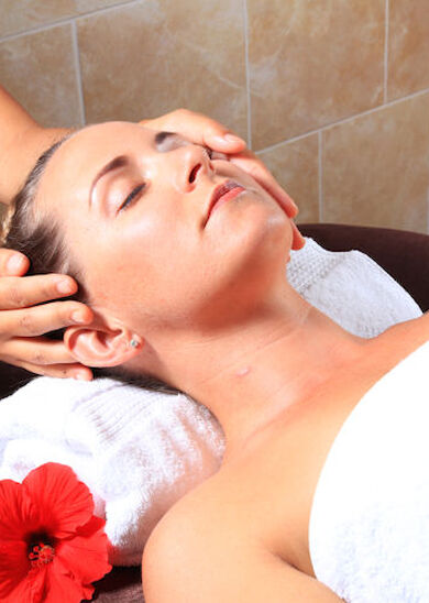 A person is receiving a head massage while lying on a towel, with a red flower placed next to their head.