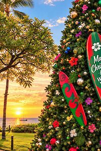 A tropical beach scene at sunset with a large decorated Christmas tree and surfboard, labeled “Magic Christmas” at Whalers Village.