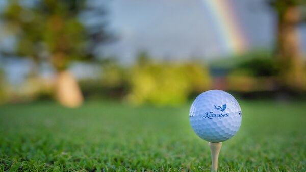 A golf ball is placed on a tee on a grassy field with a rainbow in the background.