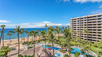 The image shows a tropical beach resort with a large hotel, multiple pools, palm trees, and beach access under a bright blue sky, ending the sentence.